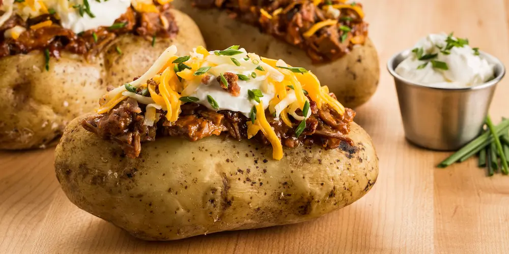 Whole baked potato split open on a plate with steam rising and a pat of butter melting into the fluffy interior