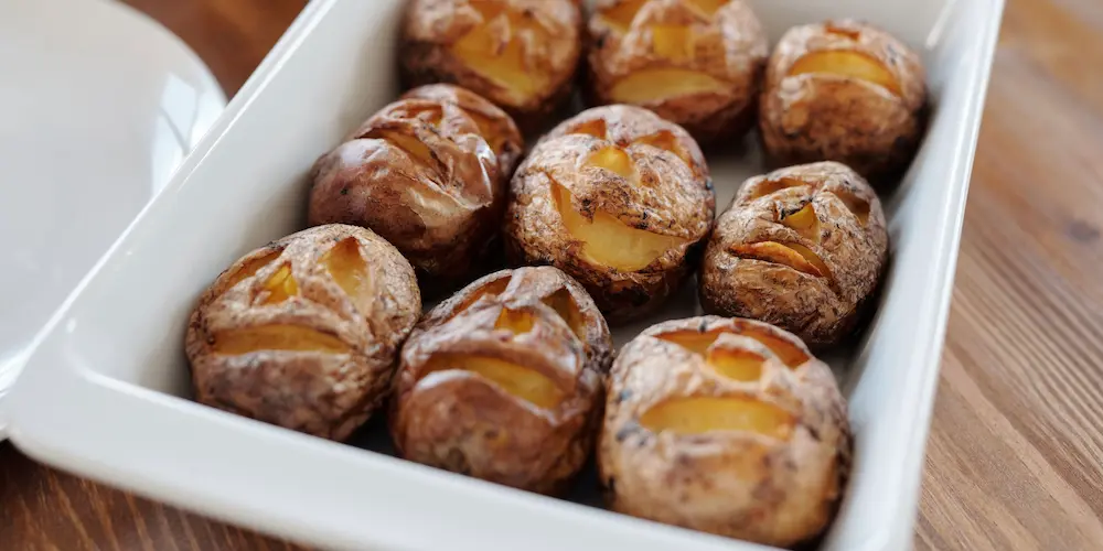 Unwrapped potatoes rubbed with oil and salt on a baking sheet, skin visibly crisping in the oven