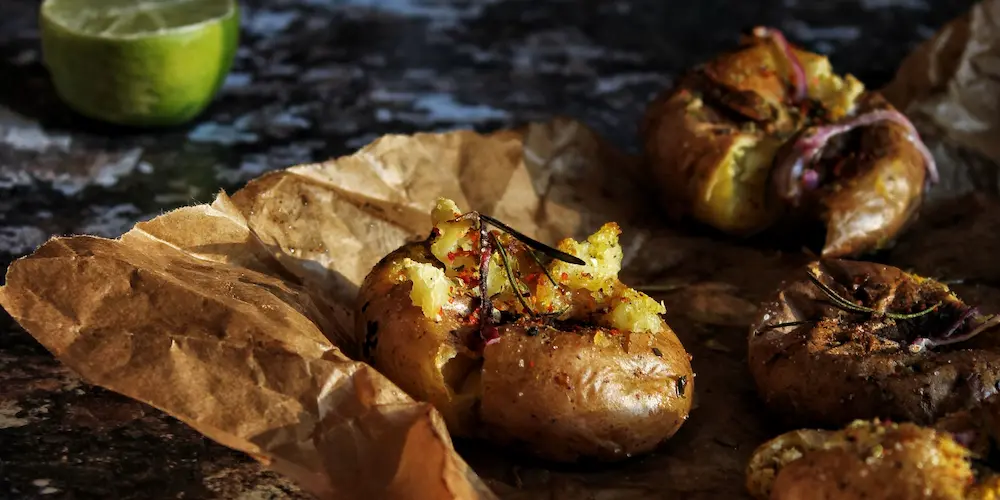 Baked potatoes cooling on a wire rack with a knife resting beside one that has been sliced open