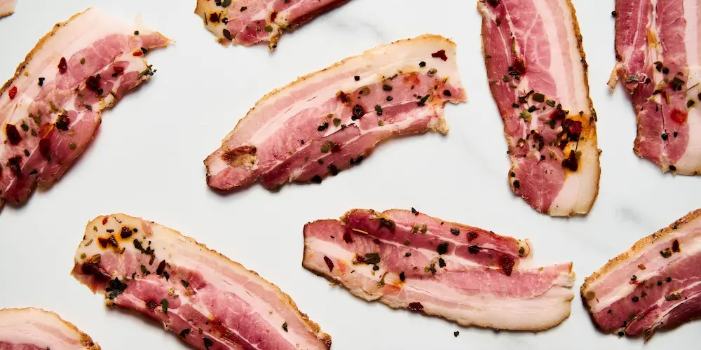 Raw bacon strips arranged on a sheet pan before placing in a cold oven