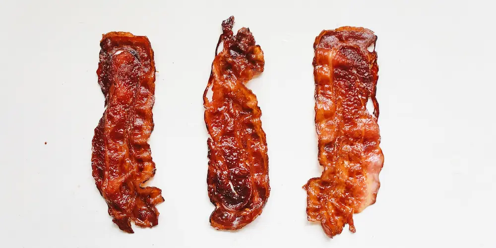 Bacon strips laid out on a wire rack over a sheet pan before baking