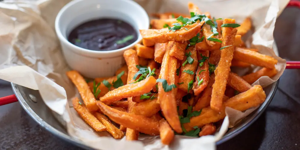 Sweet potato fries and wedges spread in a single layer on a baking sheet before going into the oven