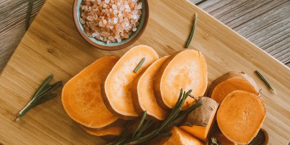 Sweet potatoes wrapped in aluminum foil next to unwrapped ones on a baking sheet before going into the oven