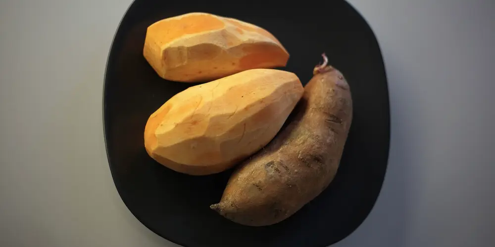 Sliced sweet potato revealing bright orange flesh next to a true yam with its rough, dark skin for comparison